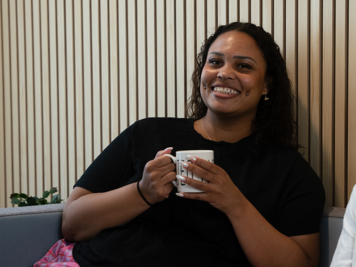 Medarbejder, der smiler til kameraret og holder en kop kaffe i begge hænder