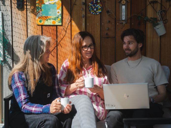 Kollegaer sidder på en terrasse og snakker omkring en bærbar computer i det der kunne være et tværfagligt samarbejde